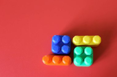 Pieces of plastic rainbow multicolored buildable toy blocks formed and arranged on red background