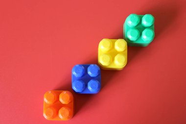 Pieces of plastic rainbow multicolored buildable toy blocks formed and arranged on red background