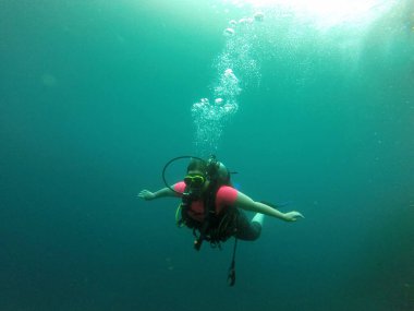 Young woman practices the sport scuba diving with oxygen tank equipment, visor, fins, relaxes and enjoys the bottom of the crystal clear water next to large branches and trunks