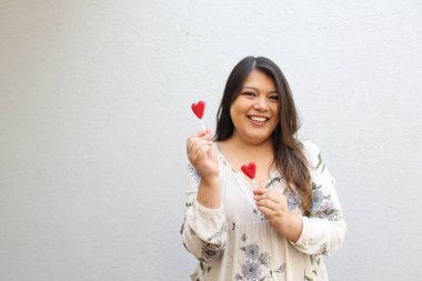 Kırmızı kalp şeklinde lolipopları olan Latin yetişkin bir kadın Şubat 'ın gelişine olan heyecanını göstermek ve sevgililer gününde ailesiyle, arkadaşlarıyla ve eşiyle sevgisini göstermek için.