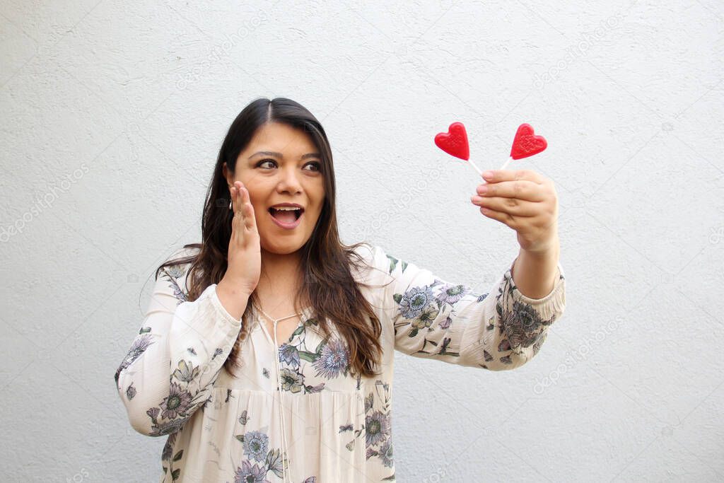 Latin adult woman with red heart-shaped lollipops to show her enthusiasm for the arrival of February and celebrate and show her affection on Valentine's Day of Love and Friendship with her family, friends and partner
