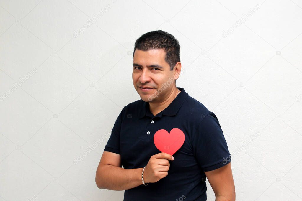 Latin adult man shows a big red heart for his enthusiasm for the arrival of February and celebrate Valentine's Day of Love and Friendship with his family, friends and partner with happiness and affection