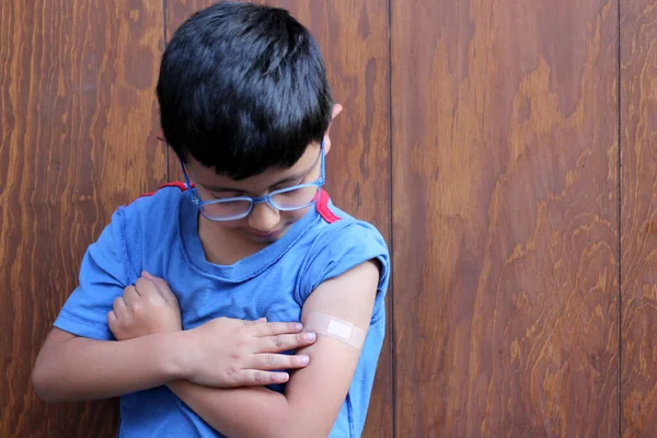 Gözlüklü ve mavi tişörtlü 6 yaşındaki küçük Latin çocuk kolunu bandajla gösteriyor çünkü Coronavirus salgınından dolayı Covid-19 'a karşı aşılanmış.