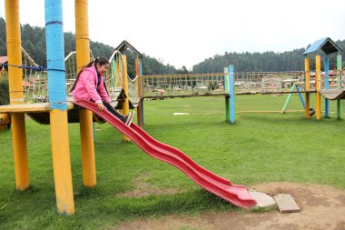 Şişman, uzun siyah düz saçlı küçük İspanyol kız açık havada kayak ve lastik salıncakları gibi renkli oyunlarda oynar.