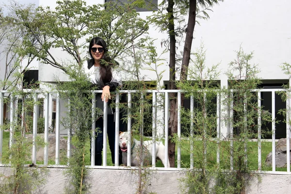 ラテン若いです大人女性とともに長いストレート黒髪は非常に満足しています彼女の友人Aホワイトピッツブル犬とともに茶色の斑点で庭を散歩屋外 — ストック写真