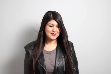 Havada uçuşan uzun düz siyah saçlı Latin yetişkin bir kadın siyah deri ceket giyen ve mutlu.