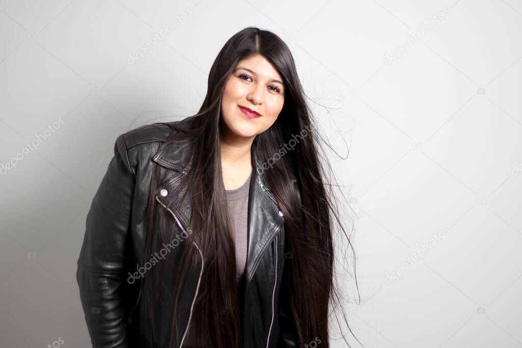 Latin adult real woman with long straight black hair that flies in the air is content and happy with her body wearing a black leather jacket