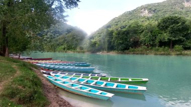 Pier with colored boats to row and walk along the river to the Tamul waterfall in Aquismn magical town of San Luis Potos, Mexico ideal for adventure sports clipart