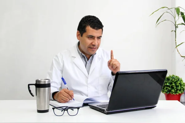 Koyu renk saçlı, beyaz önlüklü yetişkin erkek doktor, Covid-19 salgınından dolayı Coronavirus salgınının önlenmesi için uzaktan danışmanlık yapıyor.