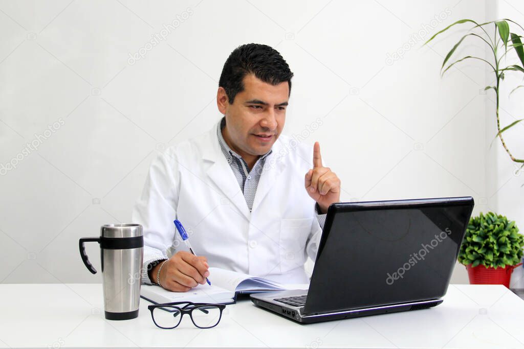Dark-haired Latino adult male doctor with white coat gives remote consultation on video call for prevention of Coronavirus contagion in the new normality due to the Covid-19 pandemic