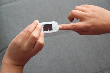 Eller, Coronavirüs salgınına bağlı yeni normallikte hastanın oksijenini ve nabzını ölçmek için oksimetrenin kullanımını gösteriyor.