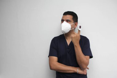 Mavi üniformalı ve yüz maskeli bir tıp doktoru parmağında oksimetrenin şüpheli Covid-19 'lu hastaların nabız ve oksijenlerini ölçmek için nasıl kullanıldığını gösteriyor.