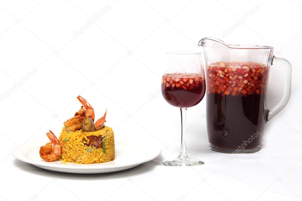 Traditional paella rice from Valencia Spain, made with saffron shellfish, shrimp and vegetables served on a white plate accompanied by red wine and a glass of clericot on a white background