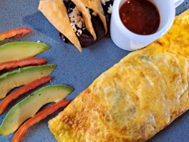 Meksika usulü omlet kahvaltısı, mantarla doldurulmuş avokado, domates, kırmızı sos, peynirli fasulye ve ahşap bir masanın yanındaki pencerenin yanında tortilla cipsi.