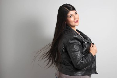 Havada uçuşan uzun düz siyah saçlı Latin yetişkin bir kadın siyah deri ceket giyen ve mutlu.