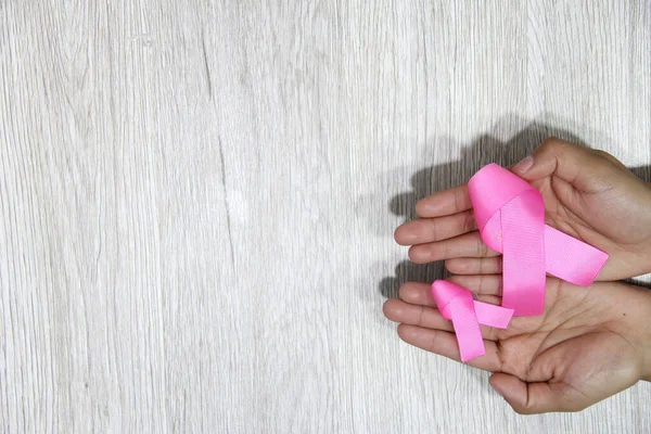 Kadın elleri ve göğüs kanserine karşı kampanya için klasik gri ahşap arka planda pembe kurdele