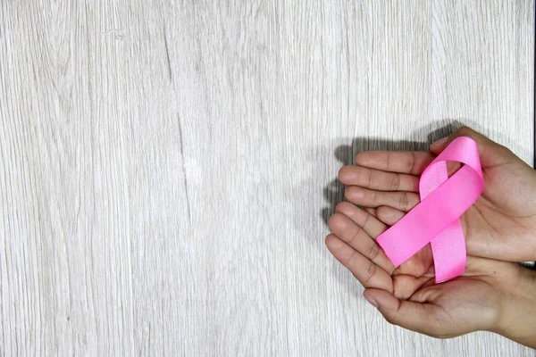 Kadın elleri ve göğüs kanserine karşı kampanya için klasik gri ahşap arka planda pembe kurdele