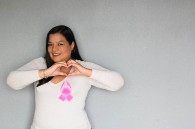 Elinde pembe kurdele olan Latin bir kadın ve göğüs kanserine karşı yürütülen kampanya için sade gri arkaplan.