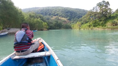 Güneş yanığı siyah saçlı Latin bir adam, San Luis Potosi Meksika 'daki Aquismon Şelalesi' ndeki berrak göl üzerinde kürek çekiyor.