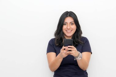 Zafer pozisyonunda cep telefonuyla izole edilmiş beyaz arka planı olan genç Latin kadın mutlu ve heyecanlı görünüyor.