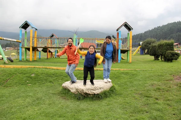 Latin family of dad, mom and daughter enjoy a picnic flying a kite and jumping with happiness for vacations and days off celebrating their love and quality time without a cell phone