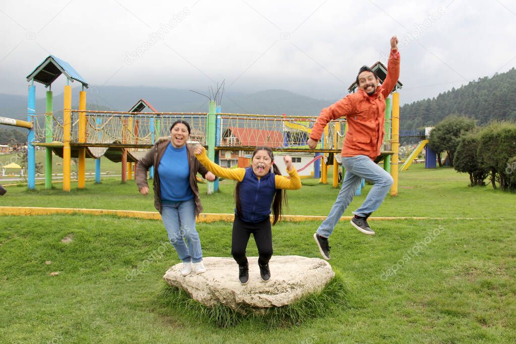 Latin family of dad, mom and daughter enjoy a picnic flying a kite and jumping with happiness for vacations and days off celebrating their love and quality time without a cell phone