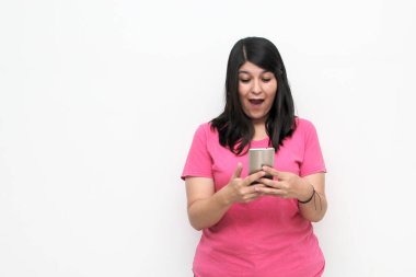 Young adult woman with black hair and pink t-shirt writes, sends and receives messages on her cell phone excitedly shopping online