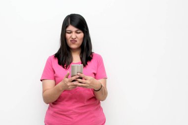 Young adult woman with black hair and pink t-shirt writes, sends and receives messages on her cell phone excitedly shopping online