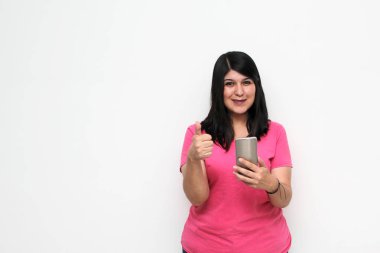 Young adult woman with black hair and pink t-shirt writes, sends and receives messages on her cell phone excitedly shopping online