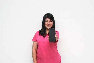 Siyah saçlı ve pembe tişörtlü genç bir kadın cep telefonundan heyecanlı bir şekilde internetten alışveriş yapıyor, mesaj gönderiyor ve alıyor.