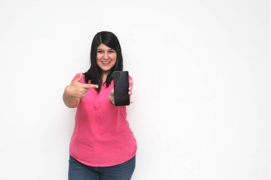 Siyah saçlı ve pembe tişörtlü genç bir kadın cep telefonundan heyecanlı bir şekilde internetten alışveriş yapıyor, mesaj gönderiyor ve alıyor.