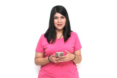 Siyah saçlı ve pembe tişörtlü genç bir kadın cep telefonundan heyecanlı bir şekilde internetten alışveriş yapıyor, mesaj gönderiyor ve alıyor.