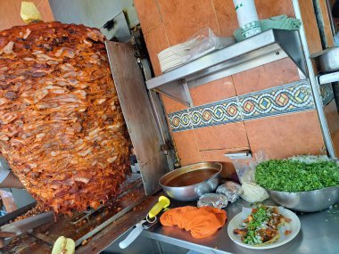 Huge top of meat for Taco al Pastor ready to be cut by the traditional Mexican taquero in Mexico City, part of the culture and delicious street cuisine with hot sauce clipart