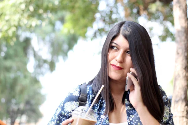 여성은 야외에서 빨대만 가지고 커피를 마시고 핸드폰을 사용하여 메시지를 보내고 — 스톡 사진