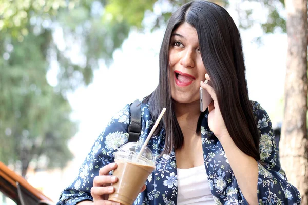 여성은 야외에서 빨대만 가지고 커피를 마시고 핸드폰을 사용하여 메시지를 보내고 — 스톡 사진