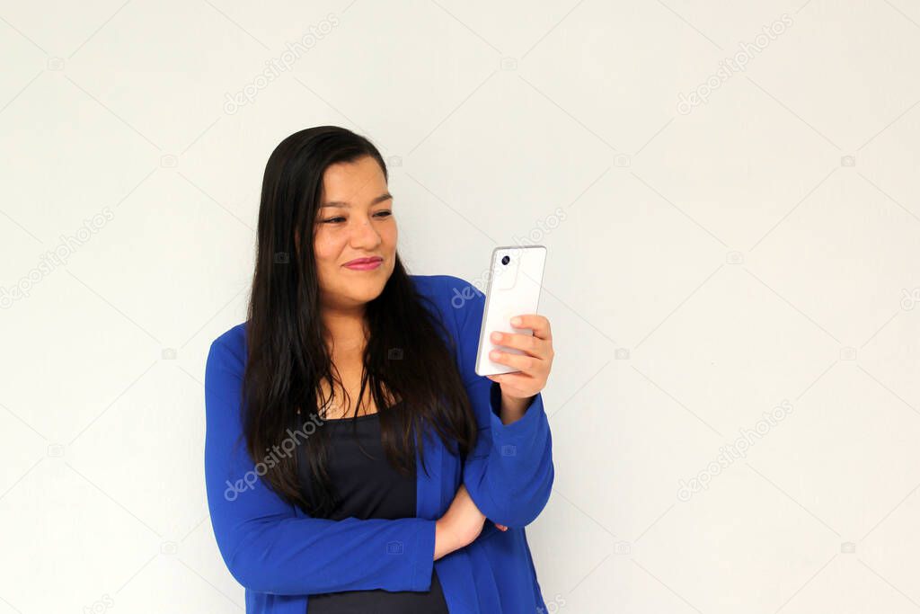 Latin adult woman with straight black hair and a blue jacket sends and receives messages from her cell phone very excited and happy makes purchases online in app