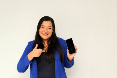 Düz siyah saçlı ve mavi ceketli Latin yetişkin bir kadın cep telefonundan çok heyecanlı ve mutlu bir şekilde internetten alışveriş yapıyor.