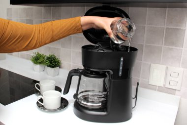 Kadınların elleri, mutfakta kahve makinesinde lezzetli ve aromatik bir kahve hazırlar. Kahvaltı için su ve taze öğütülmüş kahve.