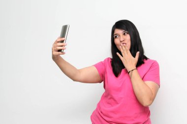 Latin yetişkin kadın, pembe bir gömlek giyerek duygu, mutluluk ve iğrenme ifadeleri içeren bir video görüşmesi yapmak için cep telefonunu kullanıyor.