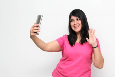 Latin yetişkin kadın, pembe bir gömlek giyerek duygu, mutluluk ve iğrenme ifadeleri içeren bir video görüşmesi yapmak için cep telefonunu kullanıyor.