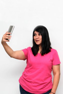 Latin yetişkin kadın, pembe bir gömlek giyerek duygu, mutluluk ve iğrenme ifadeleri içeren bir video görüşmesi yapmak için cep telefonunu kullanıyor.