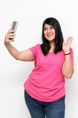 Latin yetişkin kadın, pembe bir gömlek giyerek duygu, mutluluk ve iğrenme ifadeleri içeren bir video görüşmesi yapmak için cep telefonunu kullanıyor.