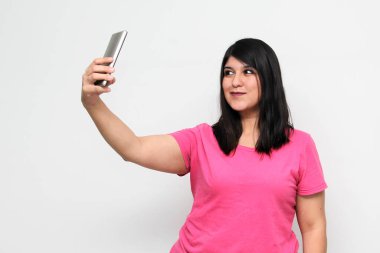 Latin yetişkin kadın, pembe bir gömlek giyerek duygu, mutluluk ve iğrenme ifadeleri içeren bir video görüşmesi yapmak için cep telefonunu kullanıyor.