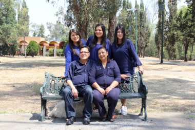 Latin aile kameraya mutlu poz veriyor ve aşk babalarıyla üç kızını mavi elbiseli bir bankta gösteriyor.