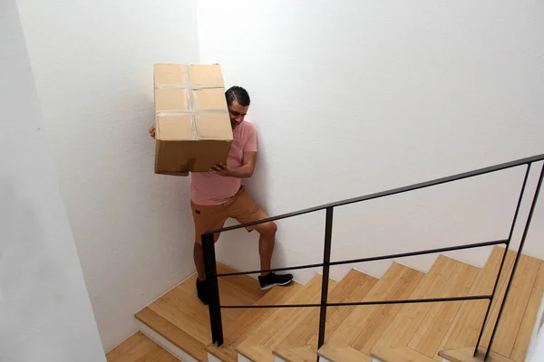 Latin adult man carries a cardboard box on the stairs of his house during a move opens house that he bought in real estate very happy for the change