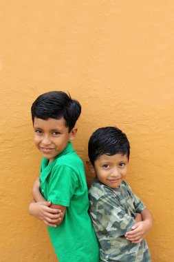 Koyu renk saçlı iki Latin erkek çocuk sarı bir duvarın önünde duruyor oyuncaksız yoksulluk içinde yaşıyorlar, hayal, oyun, mutlu bir çocukluk hayal et.