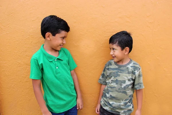 两个黑头发的拉丁男孩儿站在一道黄墙前 生活在贫困之中 没有玩具 没有梦想 没有玩耍 幻想着一个快乐的童年 — 图库照片