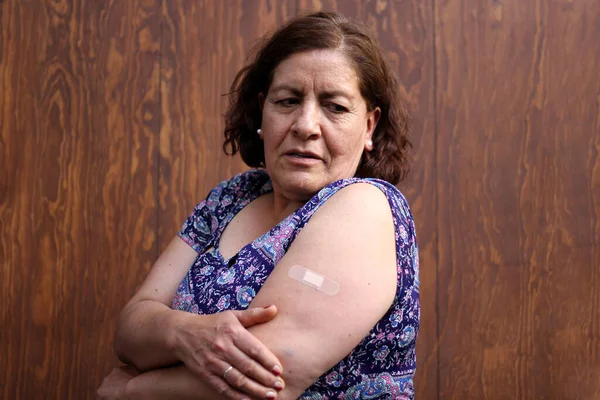 Hispanic old woman shows her arm recently vaccinated against Covid-19 in the new normal for the Coronavirus pandemic