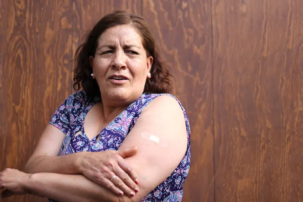 Hispanic old woman shows her arm recently vaccinated against Covid-19 in the new normal for the Coronavirus pandemic