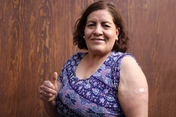 Hispanic old woman shows her arm recently vaccinated against Covid-19 in the new normal for the Coronavirus pandemic